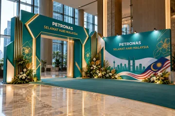 PETRONAS malaysia day celebration with a grand freestanding teal geometric entrance gateway with clear walk-through opening, Malaysian flag accents and a matching side photo wall